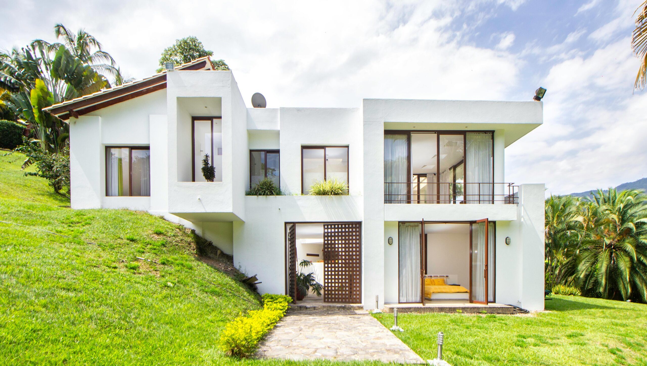 A contemporary white house surrounded by lush greenery on a hillside, showcasing modern architecture.